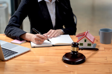 Close-up of a woman lawyer holding a pen and taking notes on a sample house mallet placed at the office desk.