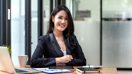 Young Asian businesswoman Beautiful smile holding a pen looking at the camera document tablet placed at the office desk.