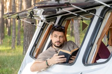 Handsome young man reading book sitting by open window of house on wheels