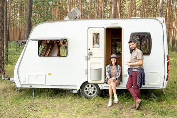 Happy young couple having rest by house on wheels among pinetrees on weekend
