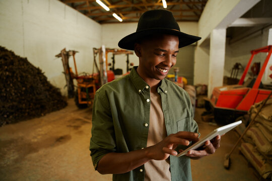 African American male farmer typing on digital tablet standing in shed