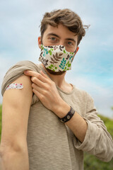 Portrait of a Caucasian young man showing arm with coronavirus vaccination patch.
