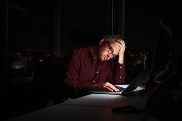 Tired and worried businessman at workplace in office holding his head on hands after late night work on laptop - obrazy, fototapety, plakaty