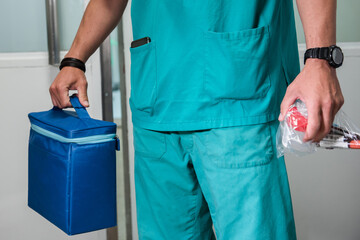 Nurse holding in one hand a blue thermal bag with samples for analysis and in the other a bottle of laboratory samples, during the coronavirus pandemic, in a hospital