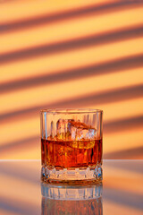 Whiskey with ice in rocks glass over striped background