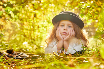 Portrait of young funny girl with blonde curly hair and in black hat in an autumn park on a yellow and orange leaf background