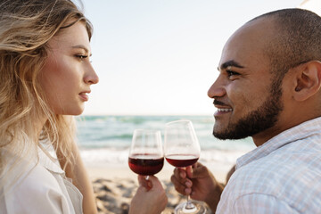 Portrait of a young couple sitting on the beach and drinking wine