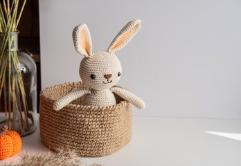 Crocheted bunny sits in a jute basket on a white background.