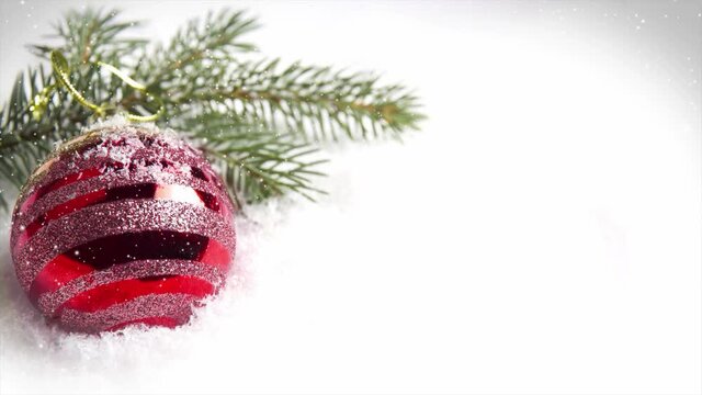 Still life with red ball on surface covered with snow. Spruce branches in the background. Falling snow effect. Calm, serene and tranquil mood. Christmas, seasonal, holiday and winter concept. High qua