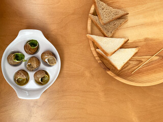 Cooked snails on a snail plate with toast on a wooden plate
