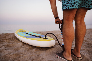 Close up of man prepares to paddle surf on a beach inflating sup board