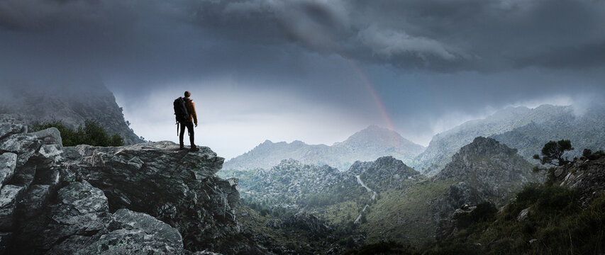 Wanderer in Berglandschaft schaut auf einen Regenbogen