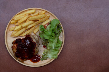 Chicken Steak with Chili Paste Sauce. Served with vegetable salad and french fries. Arranged on a round wooden plate and the floor is orange-brown tiles.