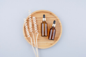 Fototapeta na wymiar Amber glass dropper bottles different sizes with metallic lid on wooden podium for product presentation. Top view on grey background with dry plants. Skincare products ,natural cosmetic.