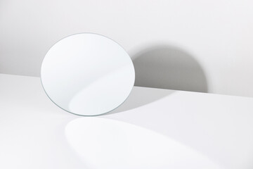 Minimalist mockup of round shaped mirror reflecting white wall placed on white table - obrazy, fototapety, plakaty