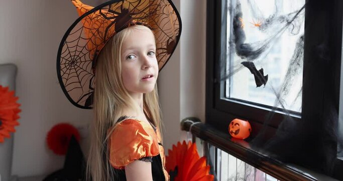 Cute Caucasian little girl with blonde hair seven years old in witch dress and hat having fun and celebrating Halloween at home during Coronavirus covid-19 pandemic and quarantine. Slow motion