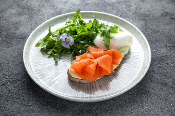 Bruschetta with salmon, poached egg and cheese. Ready menu for the restaurant. Neutral gray blue textured background