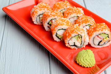 California sushi rolls served on a red plate over light wooden background. Close up, selective focus on sushi.