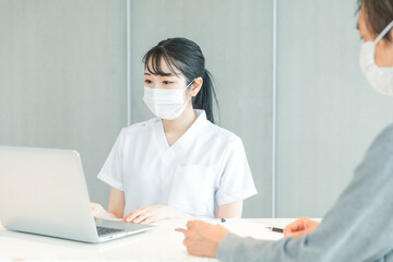 パソコンで受付する白衣の女性と患者
