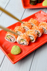 California sushi rolls served on a red plate over light wooden background. Close up, selective focus on sushi.