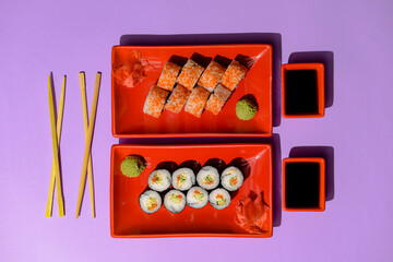 Japanese sushi rolls served on a red plate with pickled ginger and wasabi sauce over colorful purple background.