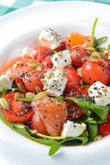 Caprese salad with mozzarella, tomato, salmon fish, basil and balsamic vinegar arranged on white plate.