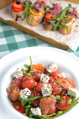 Caprese salad with mozzarella, tomato, salmon fish, basil and balsamic vinegar arranged on white plate.