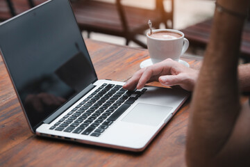 Man at cafe working on laptop computer. Male using laptop with a coffee cup on table, outdoor