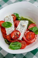 Caprese salad with strawberry, mozzarells, basil and balsamic sauce served in a white bowl over green plaid background.