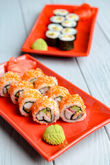 California sushi rolls served on a red plate over light wooden background. Close up, selective focus on sushi.