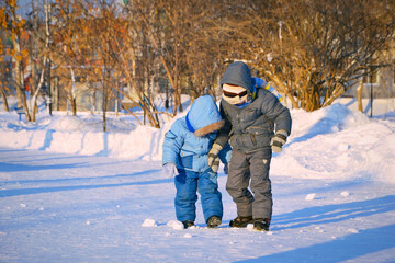 Fototapeta na wymiar Two boys trample snowballs during a winter walk on a sunny day