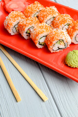 California sushi rolls served on a red plate over light wooden background. Close up, selective focus on sushi.