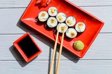 Japanese sushi rolls served on a red plate with pickled ginger and wasabi sauce over light wooden background.