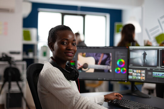 African american video editor artist looking at camera smiling editing creative video project in post production software working in startup studio office. Videographer editing audio film montage