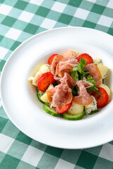 Salad with strawberry, prosciutto, herbs, cottage cheese and blackberry balsamic vinegar arranged on white plate.