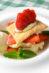 Puff pastries with strawberries and berry sauce on a white plate. Over green plaid background.
