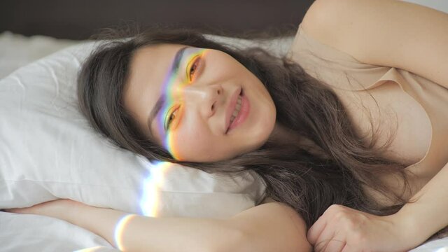 LGBT Pride Month, relationship, childbirth concept. Happy girl meets a new day. Pretty mixed race woman waking up and smiling in the morning. Rainbow flare on her face. Sun shining bright. Beauty and