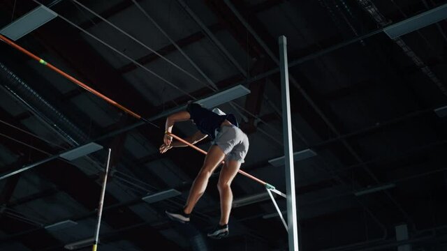 Pole Vault Jumping Championship: Professional Male Athlete Running with Pole Successfully Jumping over Bar. High Achievement Champion in Training. Cinematic Colors, Low Angle Slow Motion