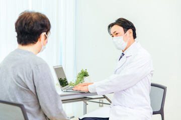 Fototapeta premium パソコンで診察するマスク姿の男性医師 