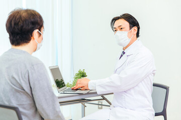 パソコンで診察するマスク姿の男性医師
