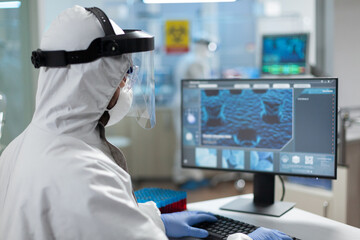Biologist researcher man wearing coronavirus protective medical equipment while typing covid19 vaccine expertise on computer during biochemistry experiment. Scientist doctor working in clinical lab