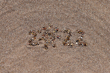 The numbers 2022 are written and lined with stones in the sand. Place for your text. Summer vacation 2022 concept