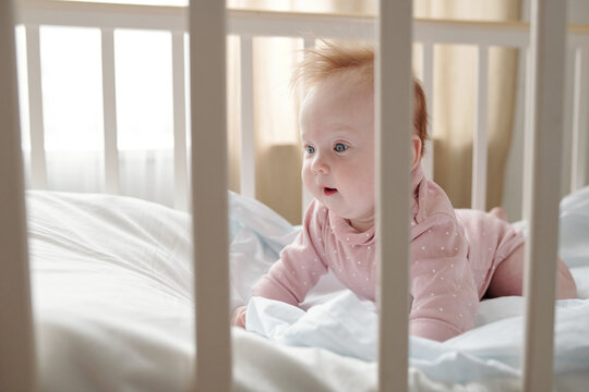 Cute baby girl crowling on white linen in her cradle after sleep