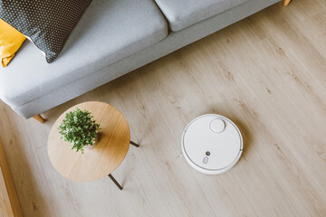 Wireless Robotic vacuum cleaner  cleaning a wooden floor in living room - obrazy, fototapety, plakaty