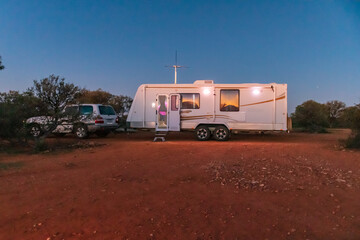 A large white caravan and four wheel drive vehicle parked in the outback of Australia at dusk. - obrazy, fototapety, plakaty