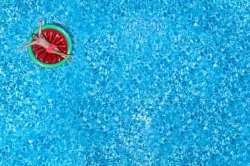 A man enjoys on a watermelon shaped float the summer sun in a big swimming pool