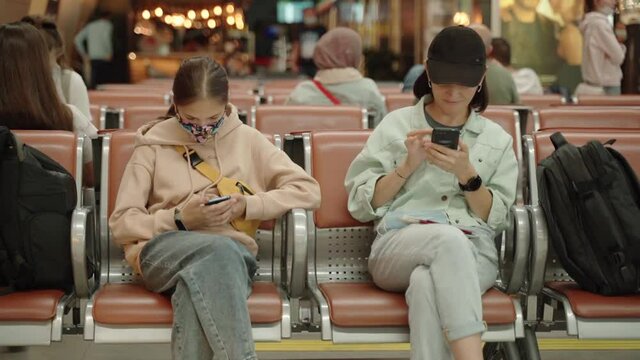 A woman and her daughter with smartphones in their hands are sitting at the airport in the waiting room.