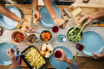 Group of friends eating together with glass of wine on dining table. Hands taking food from bowl on plate. Group of people enjoying variety of food and drinks at a getogether party