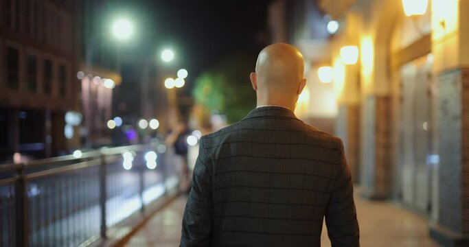 Back view bald man walking along the night city