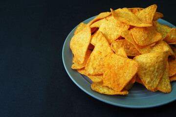 nearby, on a gray plate on a black background, there are many triangular corn tortilla chips. mexican cuisine. appetizer. side view